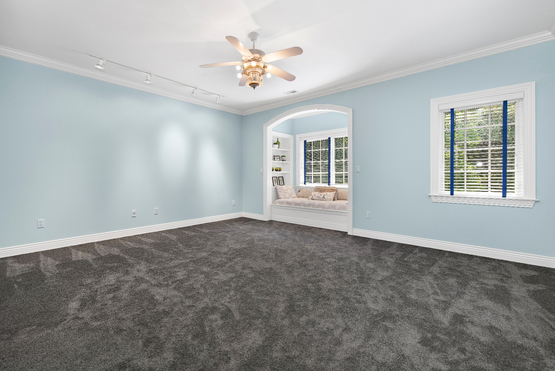 Current upper floor rec room, empty with soft blue walls, white trim, arched window-seat nook, and gray carpet