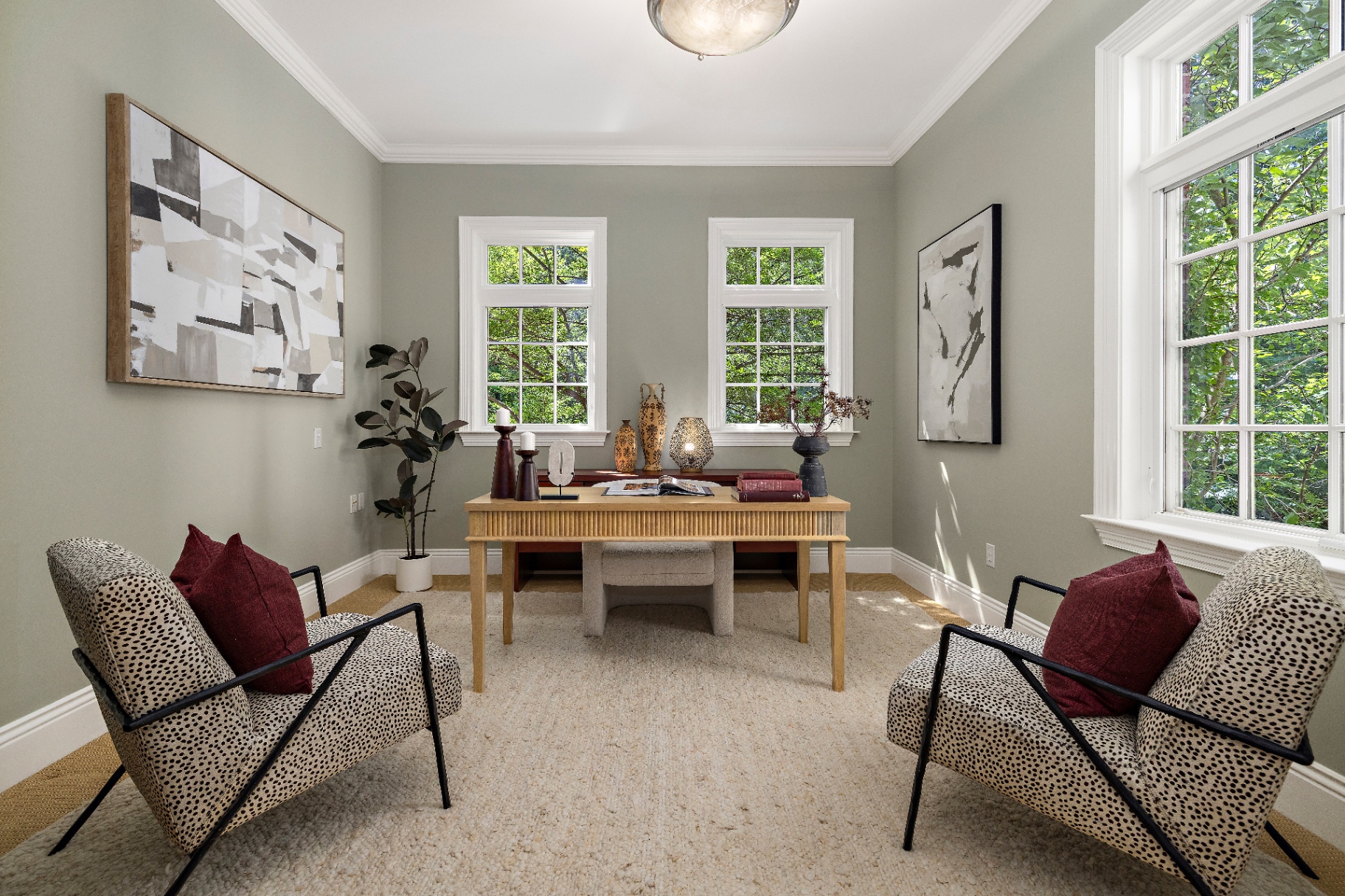 Current main floor office with sage green walls, light wood desk, cheetah-print accent chairs, and abstract art