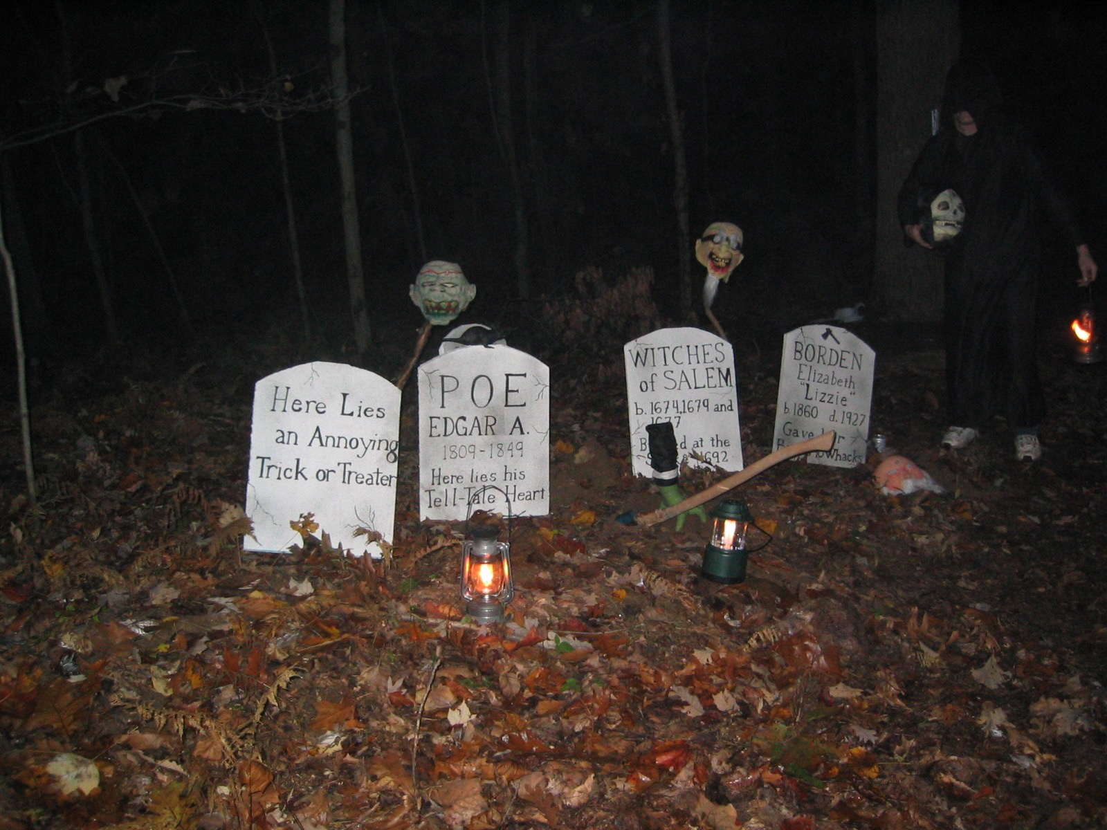Lantern-lit tombstones and costumed figures along a wooded Halloween trail at night