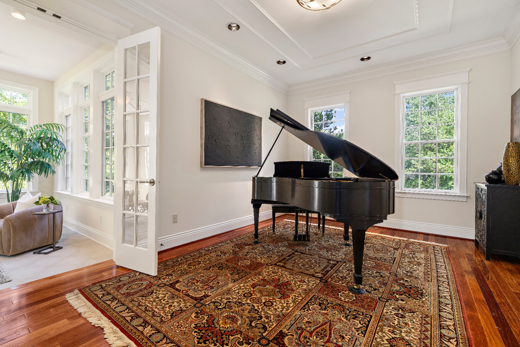 Current music conservatory with grand piano on a Persian rug, cherry hardwood floors, and windows to the sunroom